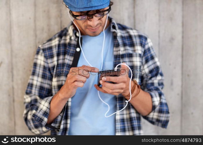 people, technology and lifestyle - close up of young hipster man with earphones and smartphone listening to music