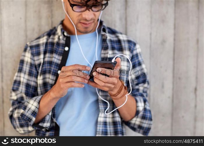people, technology and lifestyle - close up of young hipster man with earphones and smartphone listening to music
