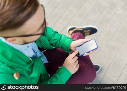 people, technology and lifestyle - close up of young hipster man with smartphone and sitting on street bench in city