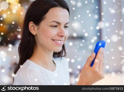 people, technology and lifestyle concept - close up of smiling young woman reading message from smartphone at cafe over snow effect