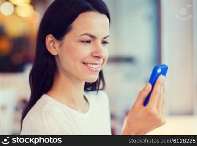 people, technology and lifestyle concept - close up of smiling young woman reading message from smartphone at cafe