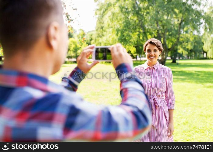 people, technology and lifestyle concept - happy couple photographing by smartphone in summer park. couple photographing by smartphone in park