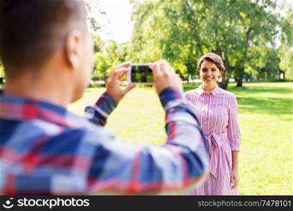 people, technology and lifestyle concept - happy couple photographing by smartphone in summer park. couple photographing by smartphone in park