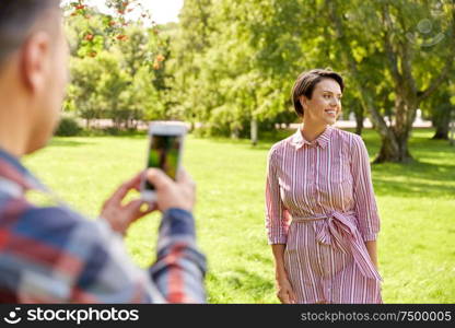 people, technology and lifestyle concept - happy couple photographing by smartphone in summer park. couple photographing by smartphone in park