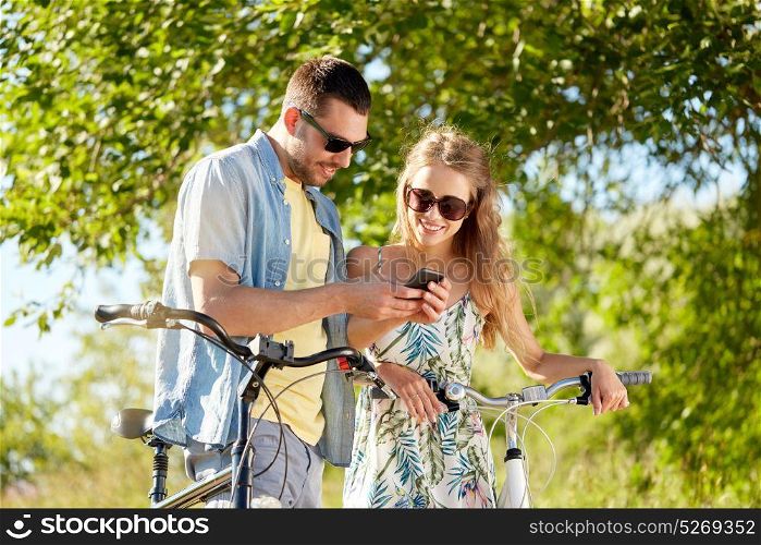 people, technology and lifestyle concept - happy couple with bicycles and smartphone at country in summer. happy couple with bicycles and smartphone outdoors
