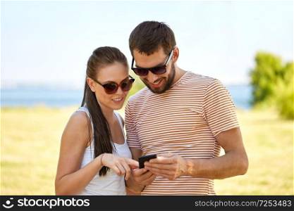people, technology and lifestyle concept - happy couple with smartphone in summer. happy couple with smartphone in summer