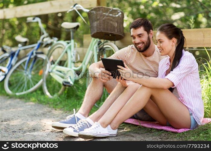 people, technology and lifestyle concept - happy couple with tablet pc computer and bicycles at summer park. couple with tablet pc and bicycles at summer park