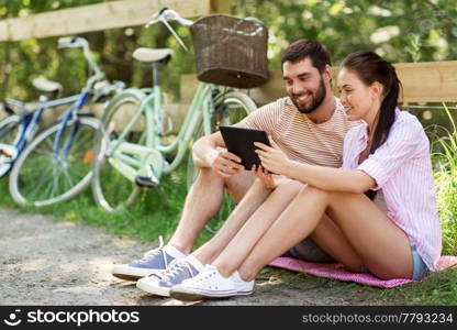 people, technology and lifestyle concept - happy couple with tablet pc computer and bicycles at summer park. couple with tablet pc and bicycles at summer park