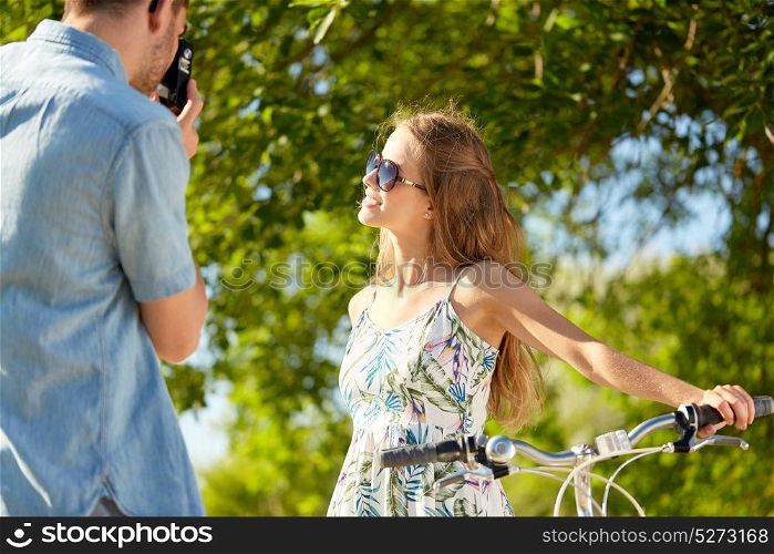 people, technology and lifestyle concept - man photographing happy woman with bicycle by camera at country in summer. man photographing woman with bicycle by camera