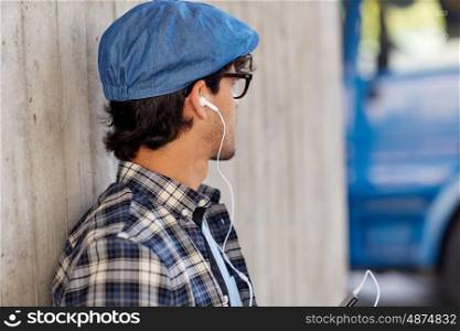 people, technology and lifestyle - happy young hipster man with earphones and smartphone listening to music