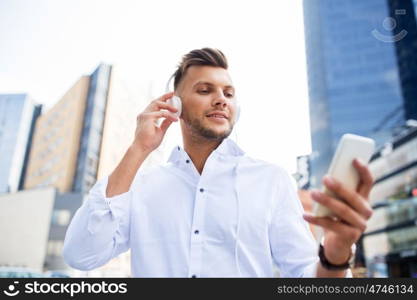 people, technology and lifestyle - happy young man with headphones and smartphone listening to music in city