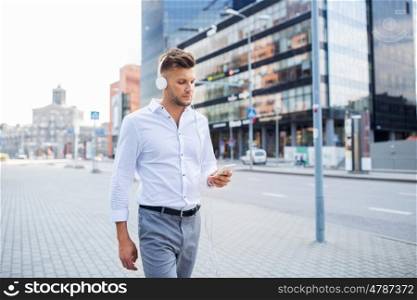people, technology and lifestyle - happy young man with headphones and smartphone listening to music in city