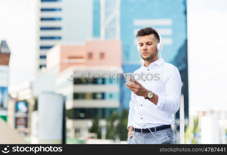 people, technology and lifestyle - happy young man with headphones and smartphone listening to music in city