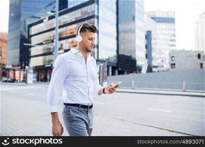 people, technology and lifestyle - happy young man with headphones and smartphone listening to music in city