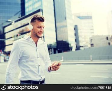 people, technology and lifestyle - happy young man with headphones and smartphone listening to music in city. man with headphones and smartphone listening music