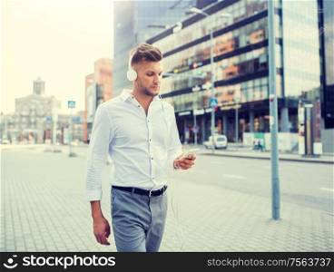 people, technology and lifestyle - happy young man with headphones and smartphone listening to music in city. man with headphones and smartphone listening music