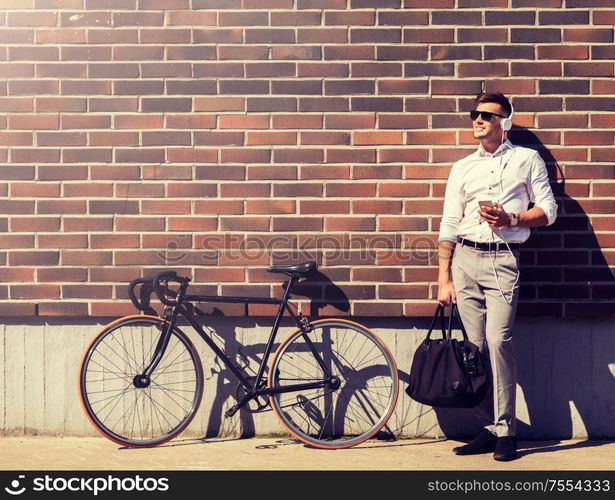 people, technology and lifestyle - happy young man with headphones, smartphone and bicycle listening to music in city. man with headphones, smartphone and bicycle