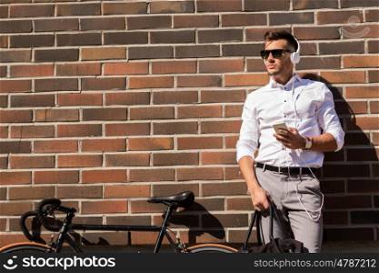 people, technology and lifestyle - young man with headphones, smartphone and bicycle listening to music in city