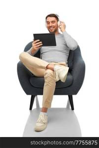 people, technology and music concept - happy smiling man with headphones and tablet pc computer sitting in chair over white background. man with headphones and tablet pc sitting in chair