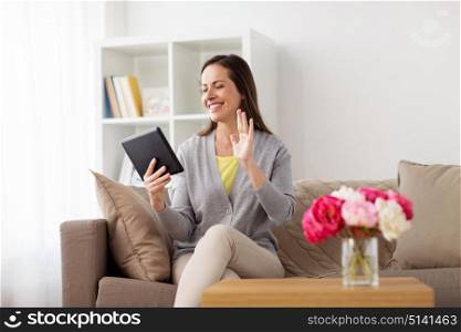 people, technology and online communication concept - happy woman sitting on sofa with tablet pc computer and having video chat at home. happy woman having video chat on tablet pc at home