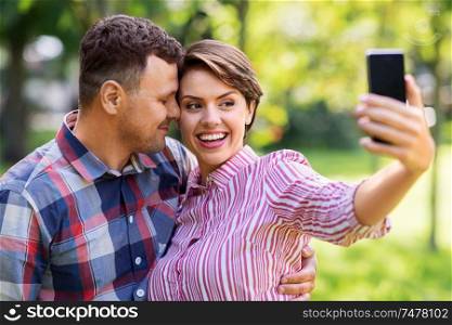 people, technology and relationships concept - happy couple in summer park taking selfie by smartphone. happy couple in park taking selfie by smartphone