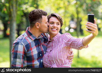 people, technology and relationships concept - happy couple in summer park taking selfie by smartphone. happy couple in park taking selfie by smartphone