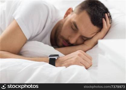 people, technology and rest concept - close up of man with smart watch sleeping in bed. close up of man with smart watch sleeping in bed