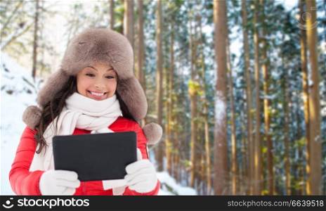 people, technology and season concept - happy smiling woman in fur hat with tablet pc computer outdoors over winter forest background. woman in fur hat with tablet pc over winter forest
