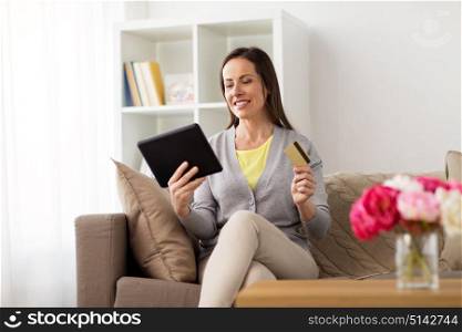 people, technology and shopping online concept - happy woman sitting on sofa with tablet pc computer and bank card at home. happy woman with tablet pc and bank card at home