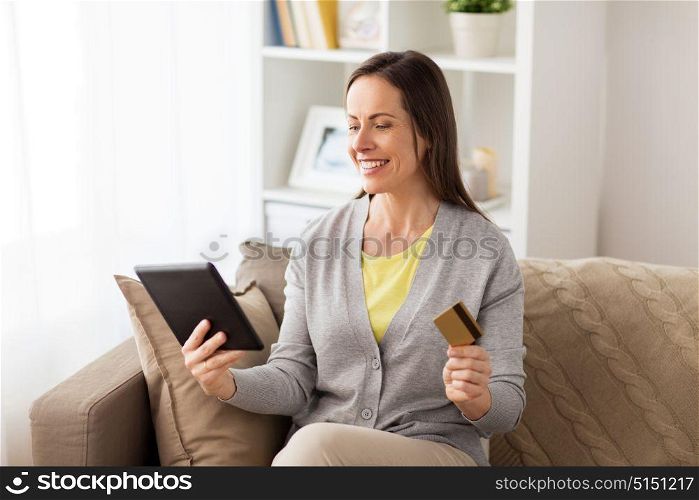 people, technology and shopping online concept - happy woman sitting on sofa with tablet pc computer and bank card at home. happy woman with tablet pc and bank card at home