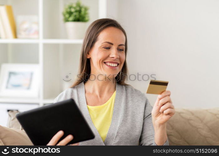 people, technology and shopping online concept - happy woman sitting on sofa with tablet pc computer and bank card at home. happy woman with tablet pc and bank card at home