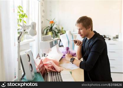 people, technology and tailoring concept - fashion designer using voice command recorder on smartphone at studio. fashion designer with smartphone working at studio