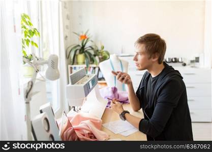 people, technology and tailoring concept - fashion designer using voice command recorder on smartphone at studio. fashion designer with smartphone working at studio