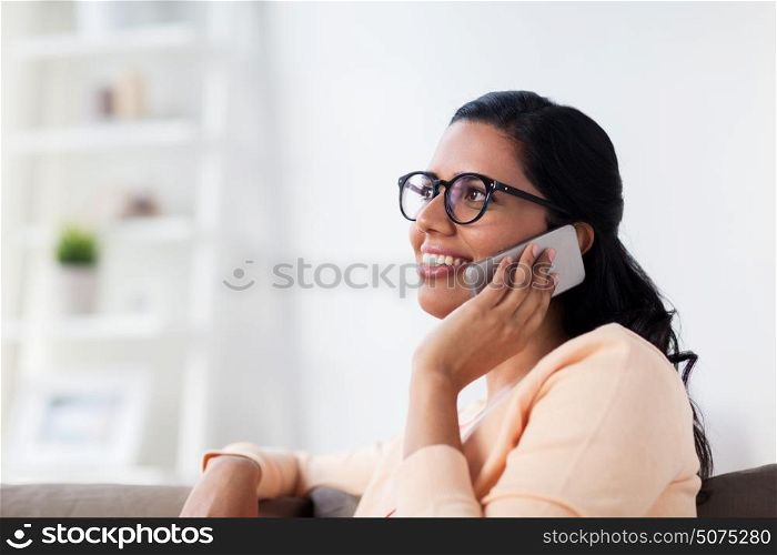 people, technology, communication and leisure concept - happy smiling young indian woman in glasses calling on smartphone at home. happy indian woman calling on smartphone at home