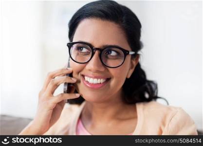people, technology, communication and leisure concept - happy smiling young indian woman in glasses calling on smartphone at home. happy indian woman calling on smartphone at home. happy indian woman calling on smartphone at home