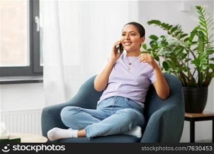 people, technology, communication and leisure concept - happy young african american woman calling on smartphone at home. african woman calling on smartphone at home