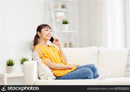people, technology, communication and leisure concept - happy young asian woman calling on smartphone at home
