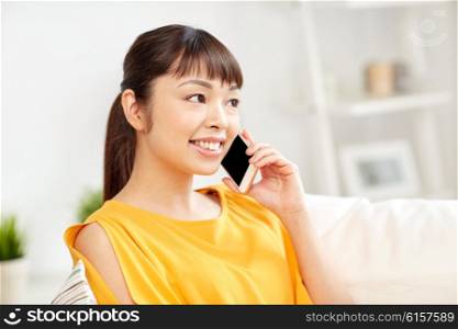 people, technology, communication and leisure concept - happy young asian woman calling on smartphone at home