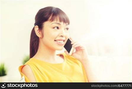 people, technology, communication and leisure concept - happy young asian woman calling on smartphone at home. happy asian woman calling on smartphone at home. happy asian woman calling on smartphone at home