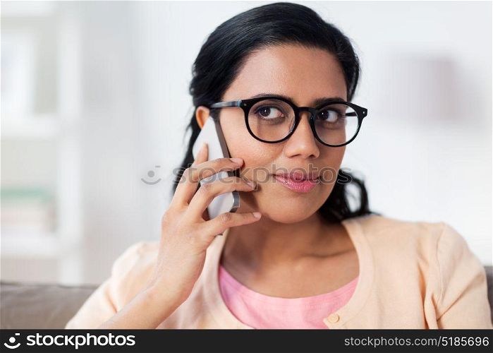 people, technology, communication and leisure concept - happy young indian woman in glasses calling on smartphone at home. happy indian woman calling on smartphone at home