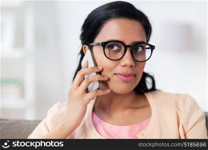 people, technology, communication and leisure concept - happy young indian woman in glasses calling on smartphone at home. happy indian woman calling on smartphone at home