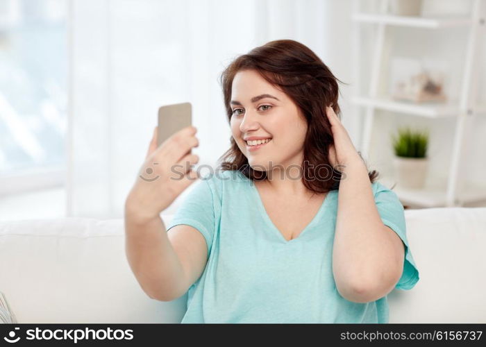 people, technology, communication and leisure concept - happy young plus size woman taking selfie with smartphone at home