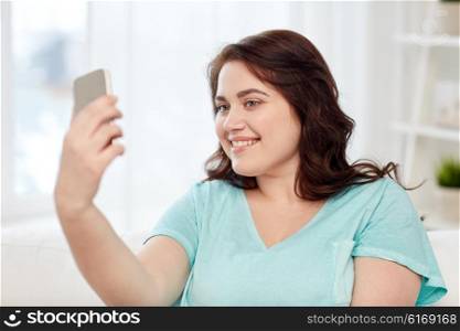 people, technology, communication and leisure concept - happy young plus size woman taking selfie with smartphone at home