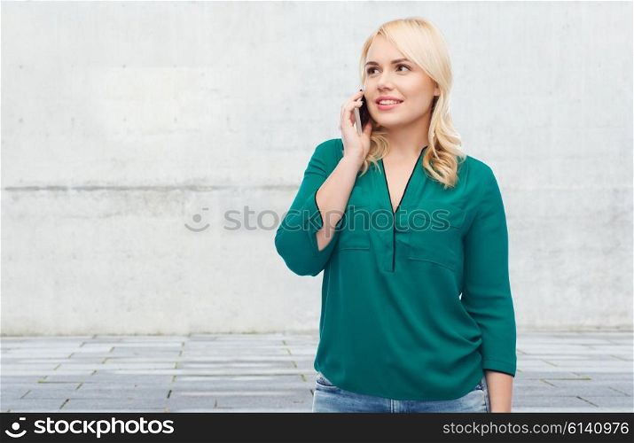 people, technology, communication and leisure concept - happy young woman calling on smartphone over gray concrete wall background