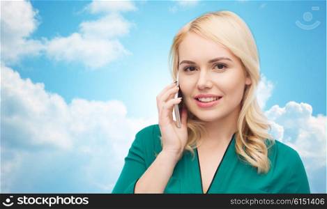 people, technology, communication and leisure concept - happy young woman calling on smartphone over blue sky and clouds background