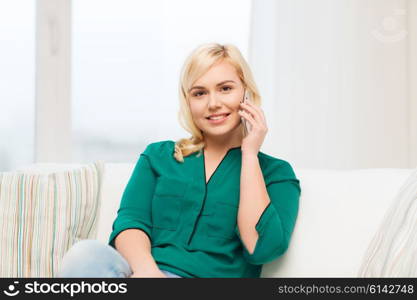 people, technology, communication and leisure concept - happy young woman calling on smartphone at home