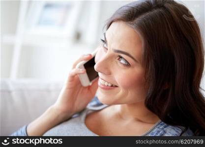 people, technology, communication and leisure concept - happy young woman calling on smartphone at home