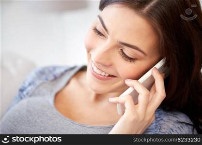 people, technology, communication and leisure concept - happy young woman calling on smartphone at home