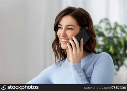 people, technology, communication and leisure concept - happy young woman calling on smartphone at home. smiling woman calling on smartphone at home