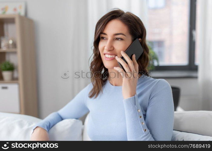 people, technology, communication and leisure concept - happy young woman calling on smartphone at home. smiling woman calling on smartphone at home